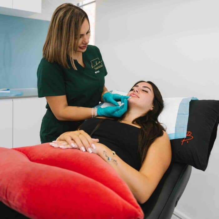 Client receiving lip filler treatment at a cosmetic clinic to enhance lip volume and shape.